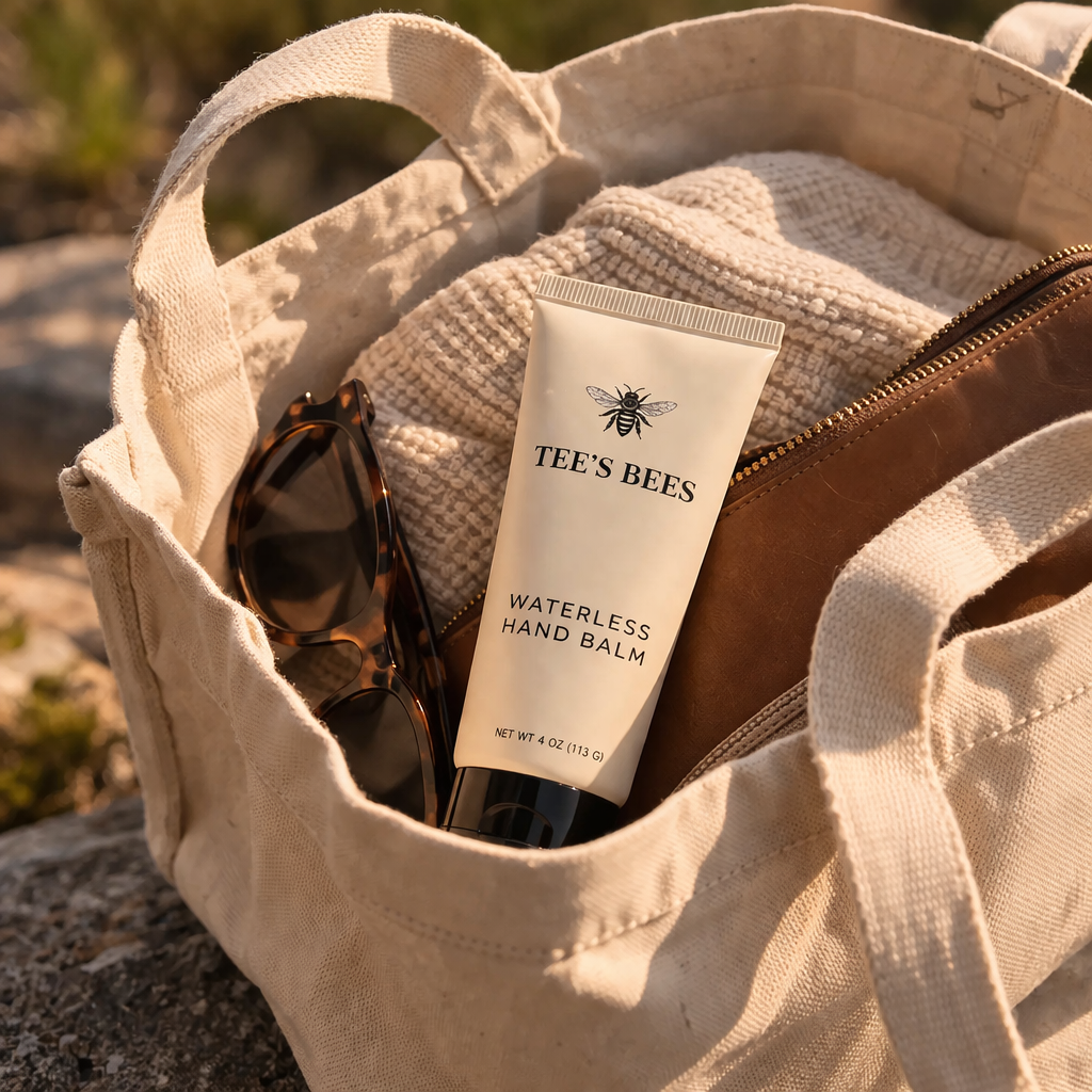 Tee's Bees waterless hand balm in a beige bag with sunglasses and a towel.