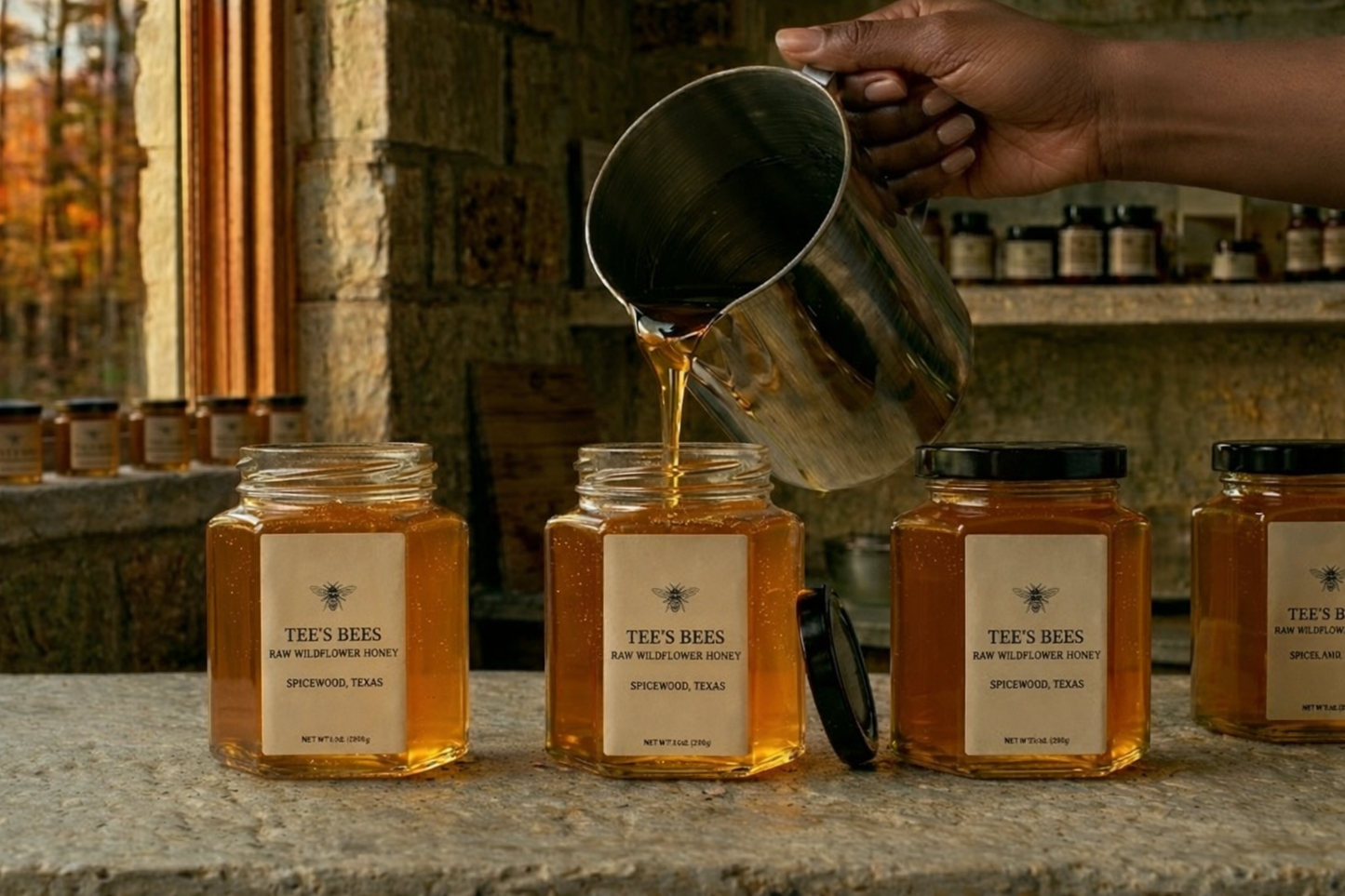 Honey being poured from a metal jar into jars labeled 'Tee's Bees' with a rustic background.